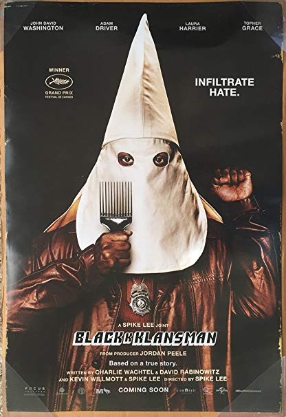 A black man wearing a Ku Klux Klan hood holds up his fist