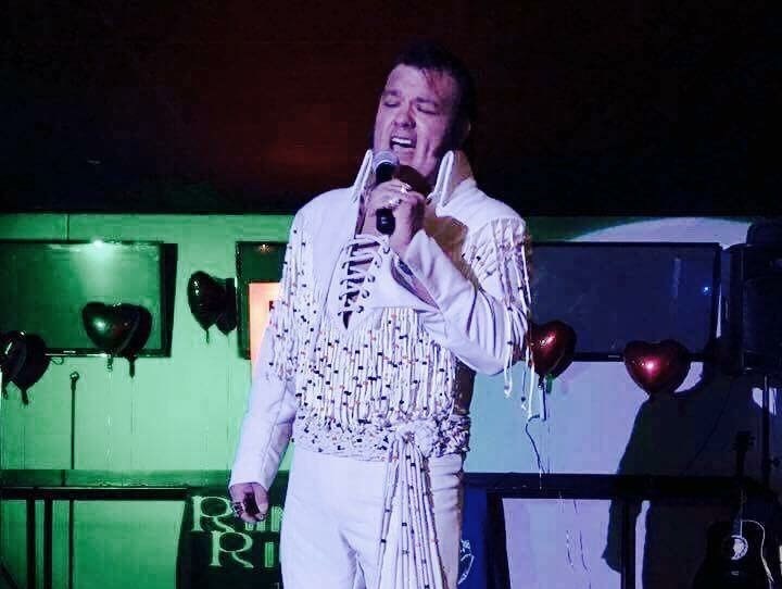 Image of Elvis Tribute Artist singing into a microphone onstage.