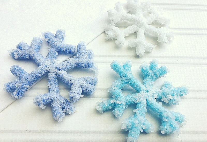 Three snowflakes of varying shades of blue coated in borax crystals