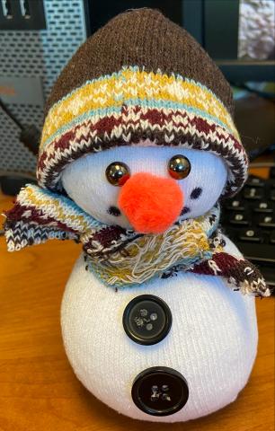 Small sock snowman with patterned sock as hat and scarf. Button on belly and eyes. Fuzzy orange nose and dotted smile.