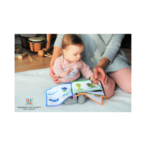 Young infant sitting on floor with book and mother holding it