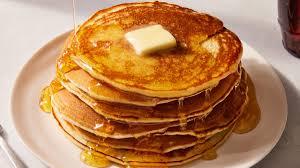Stack of fresh pancakes with butter melting on it and syrup pouring over sides.